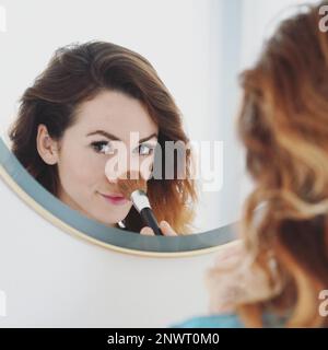 Junge Frau ihre Nase pudern mit Make-up-Pinsel, Badezimmerspiegel, Portrait mit selektiven Fokus Stockfoto