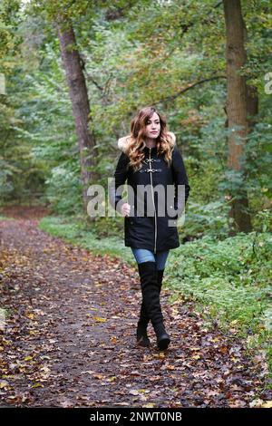 Junge Frau tragen Winter Mantel und Overknee Stiefel auf einsamen Waldweg im Herbst Stockfoto