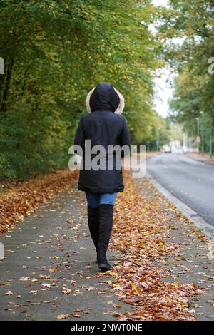 Ansicht der Rückseite des unkenntlich Frau Winter Mantel und Stiefel zu Fuß die Straße im Herbst Stockfoto