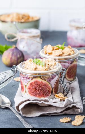 Hausgemachter gesunder Joghurt in Glastopf mit Müsli, Feigen, Minze auf rustikalem Betonhintergrund. Gesundes Frühstück am Morgen. Frisch zubereiteter Joghurt mit Stockfoto