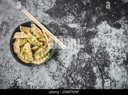 Asiatische Knödel in der Schüssel, Essstäbchen, rustikaler Steinhintergrund. Draufsicht. Platz für Text. Chinesische Knödel zum Abendessen. Nahaufnahme. Speicherplatz kopieren. Stockfoto