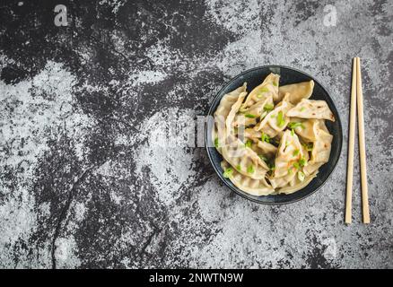 Asiatische Knödel in der Schüssel, Essstäbchen, rustikaler Steinhintergrund. Draufsicht. Platz für Text. Chinesische Knödel zum Abendessen. Nahaufnahme. Speicherplatz kopieren. Stockfoto