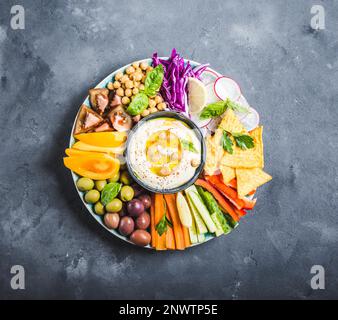 Hummus-Platte mit verschiedenen Snacks. Hummus in der Schüssel, Gemüsestangen, Kichererbsen, Oliven, Pita-Chips. Teller mit Meze aus nahöstlichem/mediterranem Raum. Stockfoto