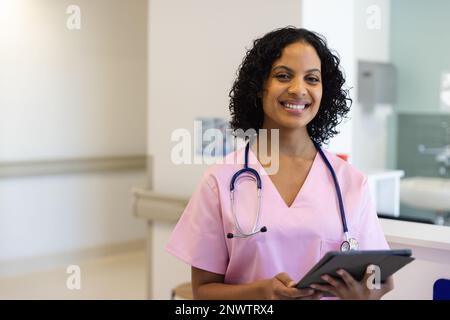 Porträt einer glücklichen birassischen Ärztin mit Stethoskop mit Tablette im Krankenhaus. Gesundheits-, Krankenhaus- und Pflegekonzept. Stockfoto