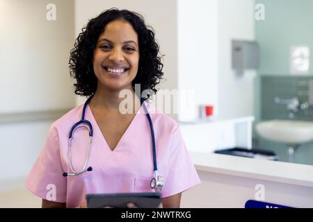 Porträt einer glücklichen birassischen Ärztin mit Stethoskop mit Tablette im Krankenhaus. Gesundheits-, Krankenhaus- und Pflegekonzept. Stockfoto
