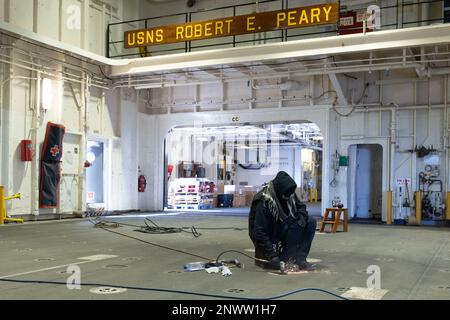 NORFOLK, Virginia (6. Februar 2023) Military Sealift Command Civil Service Mariner, Able Seaman Vanessa White, verwendet eine Schleifmaschine, um an Bord des Trockenfrachtschiffs USNS Robert E. Peary der Lewis- und Clark-Klasse Farbe von einem Padeye zu entfernen (T-AKE 5) Während das Schiff im Atlantik unterwegs ist, um Seeversuche am 6. Februar 2023 durchzuführen. Stockfoto