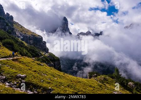 Drei Wanderer auf einem Pfad in den Brenta-Dolomiten, teilweise von Wolken umhüllte Gipfel in der Ferne. Stockfoto