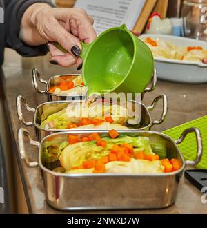 Der Koch gießt Sauce auf Kohlbrötchen mit Lachs und Karotten in der Küche. Französisches Rezept Stockfoto