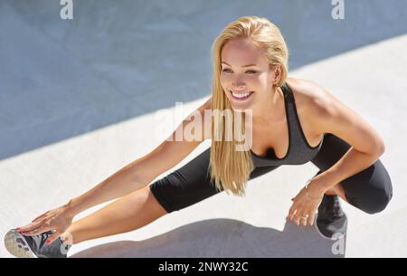 Sie ist unglaublich flexibel. Eine lange Aufnahme einer jungen Frau, die sich draußen die Beine ausstreckt. Stockfoto