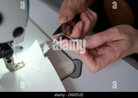 Nahaufnahme der Hände eines professionellen Schneiders oder Schneiders, der Fäden mit einer scharfen Schere schneidet, nachdem er Lederteile zusammengenäht hat Stockfoto