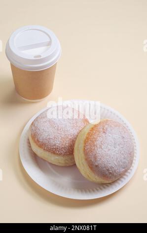 Berliner Donuts auf einem Pappteller und ein Glas Kaffee auf hellbraunem Hintergrund. Umweltfreundliche Einwegschalen zum Mitnehmen Stockfoto