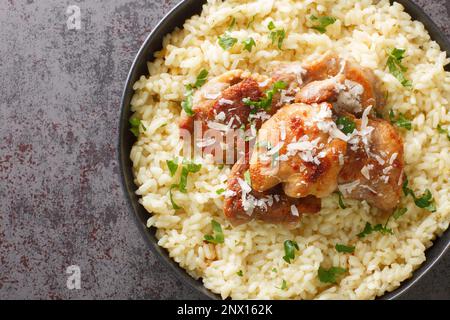 Arborio-Reis mit Parmesan und Knoblauch, serviert mit gebratenem Hähnchen in Nahaufnahme auf einem Teller auf dem Tisch. Horizontale Draufsicht von oben Stockfoto