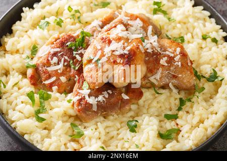 Arborio-Reis mit Parmesan und Knoblauch, serviert mit gebratenem Hähnchen in Nahaufnahme auf einem Teller auf dem Tisch. Horizontal Stockfoto