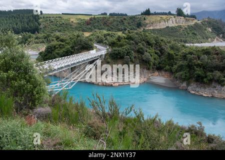 Das leuchtend blaue Wasser der Rakaia River Gorge in Neuseeland, während das Wasser unter einer weißen Brücke fließt. Stockfoto