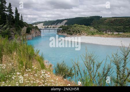 Die Rakaia River Gorge und die umliegende Landschaft, eine historische Brücke führt über das blaue Wasser, bestehend aus Gletscherschmelzwasser in Neuseeland. Stockfoto