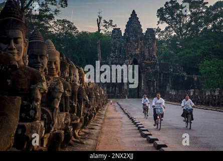 Frauen, Radsport, Brücke und Südtor von Angkor Thom, Angkor, Siem Reap, Kambodscha Stockfoto