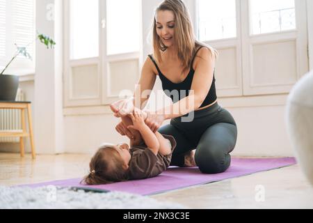 Eine junge Frau passt mom und ein kleines Mädchen, das zu Hause auf der Matte trainiert Stockfoto