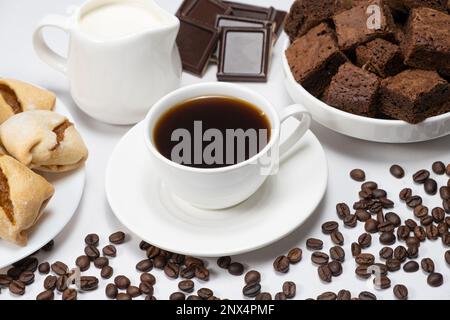 Kaffeekeramantasse mit Milchkanne, Kuchen, Schokolade und Kaffeebohnen auf weißem Hintergrund Stockfoto