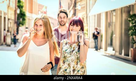 Junger Mann, der hübschen Frauen folgt und gleichzeitig Spaß auf der Straße hat - Technologiekonzept im Alltag mit Millennials-Leuten, die reden Stockfoto