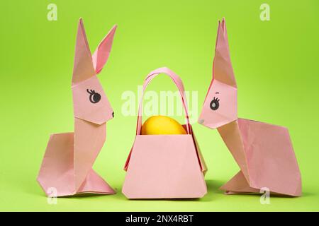 Oster-Origami - zwei Papierhasen und ein Ei mit grünem Hintergrund. Basteln für die Feiertage, machen Sie es selbst. Stockfoto