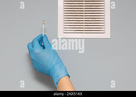 Man prüft den Zustand des Lüftungsgitters. Ein Mann, der den Lüftungsgitter im Zimmer reinigt. Heimbelüftung Desinfektion. Hand haltende Baumwolle Stockfoto