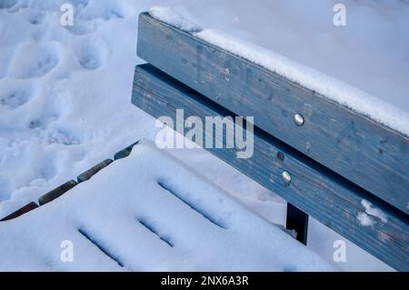 Hellblaue Holzbank mit Schnee in einem öffentlichen Park in Finnland. Winter im Park. Fußspuren im Schnee. Einfache Bank. Kaltes Wetter. Stockfoto