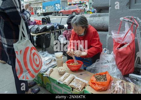 Eine ältere amerikanische Frau aus dem Kino verkauft Kräuter und scheinbar Nüsse im Freien auf der Main Street in Chinatown, Flushing, Queens, New york City. Stockfoto