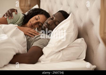 Ein junges, multirassisches Paar schläft morgens im Bett Stockfoto