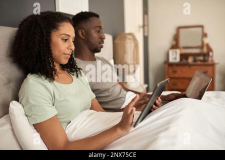 Multirassisches Paar, das morgens im Bett verschiedene Geräte benutzt Stockfoto