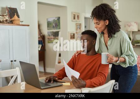 Lächelndes, multiethnisches Paar, das seine Rechnungen zu Hause online bezahlt Stockfoto