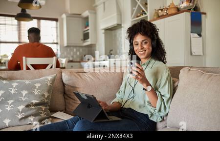 Lächelnde Frau, die Kopfhörer trägt und ein Tablet auf ihrem Sofa verwendet Stockfoto