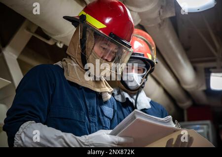 Elektriker Mate 3. Klasse Alan Posadas, Left, und Seaman Cody Spiegel, dem Amphibien-Transportschiff USS Arlington (LPD 24) der San Antonio-Klasse zugewiesen, überprüfen eine Checkliste während einer allgemeinen Quartierübung, die im Atlantik durchgeführt wird, am 10. Februar 2023. Arlington-Matrosen halten die Schadenskontrolle durch Routineübungen sowohl im Hafen als auch unterwegs aufrecht. Stockfoto