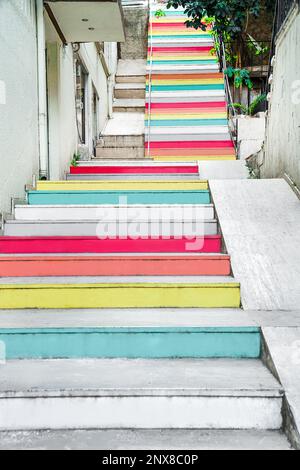 Die Treppen sind mit mehrfarbigen Farben gestrichen, steigen auf eine enge Straße, Blick von unten, Konzept der positiven Einstellung Stockfoto