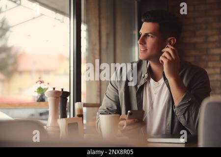 Mann mit Smartphone, der Hörbuch am Tisch im Café hört Stockfoto