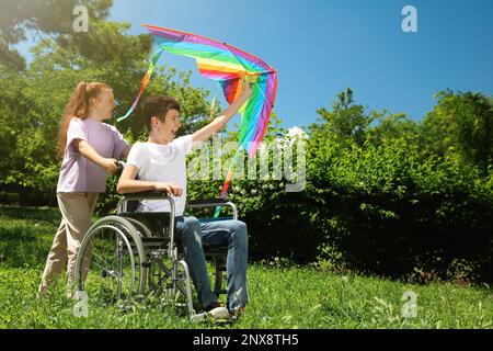 Glücklicher Teenager im Rollstuhl mit Drachen und Mädchen im Park an sonnigen Tagen Stockfoto