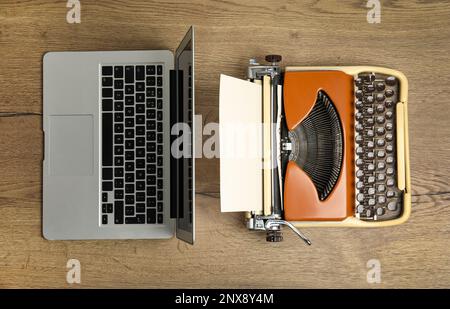 Alte Schreibmaschine und Laptop auf Holztisch, flach liegend. Konzept des technischen Fortschritts Stockfoto