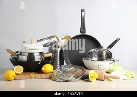 Set aus sauberem Küchengeschirr und Zitronen auf Holztisch vor hellem Hintergrund Stockfoto