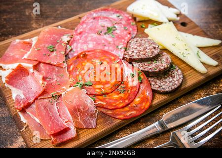 Italienische Küche: Ein Holzbrett mit verschiedenen Aufschnitten und Gourmetkäsen, darunter Parmaschinken, Salami und Chorizo. Stockfoto