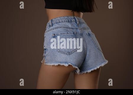 Schlanke Frau mit glatter Haut in Denim-Shorts auf beigem Hintergrund, Nahaufnahme. Cellulitenproblem-Konzept Stockfoto