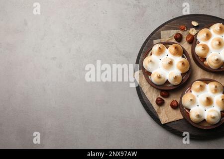 Köstliche gesalzene Karamellschokoladentörtchen mit Baiser und Haselnüssen auf grauem Tisch, Draufsicht. Platz für Text Stockfoto