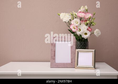 Leere Bilderrahmen und schöner Blumenstrauß auf weißem Tisch nahe der rosafarbenen Wand, Platz für Text Stockfoto