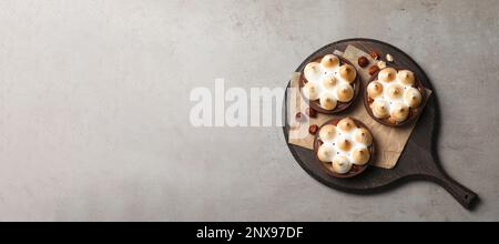 Köstliche gesalzene Karamellschokoladentörtchen mit Baiser und Haselnüssen auf grauem Tisch, Draufsicht. Platz für Text Stockfoto