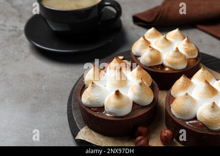 Köstliche Karamell-Schokoladentörtchen mit Baiser und Haselnüssen auf grauem Tisch, Nahaufnahme Stockfoto