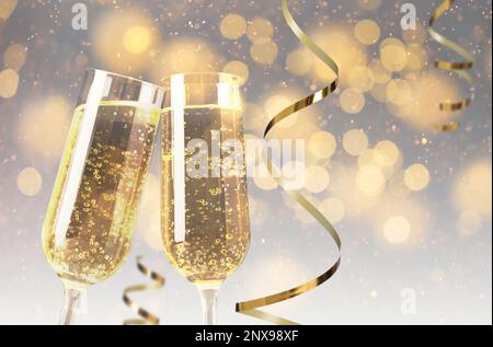 Gläser mit Sekt und glänzenden Schlangenschnüren gegen verschwommenes festliches Licht Stockfoto