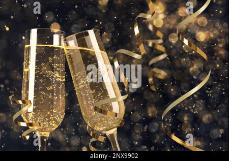 Gläser mit Sekt und glänzenden Schlangenschnüren gegen verschwommenes festliches Licht Stockfoto