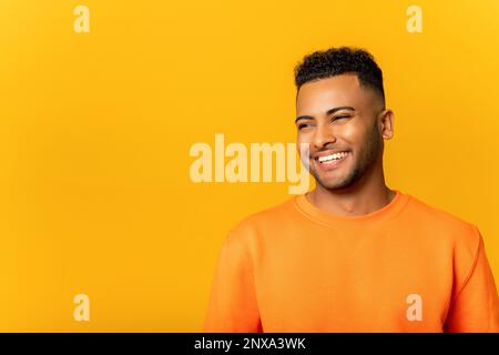 Portrait eines glücklichen, zufriedenen, gutaussehenden jungen Indianers, der mit einem Lächeln steht und wegschaut. Innenaufnahmen im Studio auf gelbem Hintergrund Stockfoto