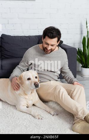 Labrador-Hund liegt auf dem Teppich in der Nähe eines glücklichen bärtigen Mannes, Stockbild Stockfoto