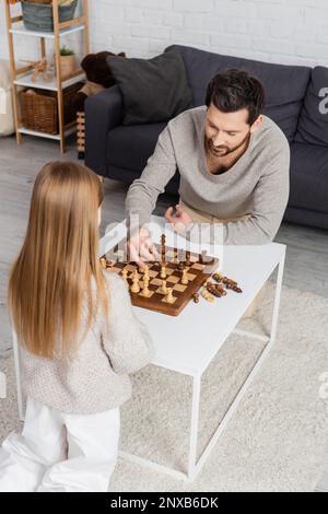 Blick aus einem hohen Winkel auf einen bärtigen Mann, der Schach mit einer jungen Tochter zu Hause spielt, Stockbild Stockfoto