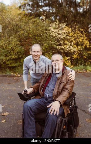 Porträt eines lächelnden jungen Mannes mit Arm um den Vater im motorisierten Rollstuhl Stockfoto