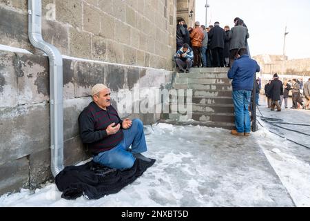 Ein muslimischer Mann legte seinen Mantel auf den verschneiten Boden und setzte sich darauf und betete, wenn in der Moschee kein Platz mehr ist. Erzurum, Türkei. Stockfoto